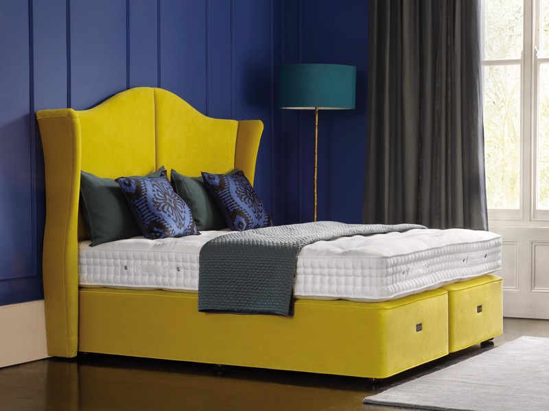 A yellow bed base with a naked mattress on it, save for a throw