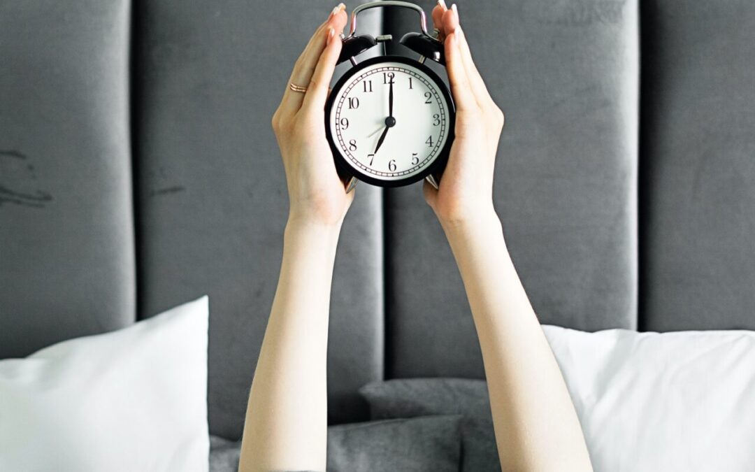 Two hands lifting an alarm clock in the air.