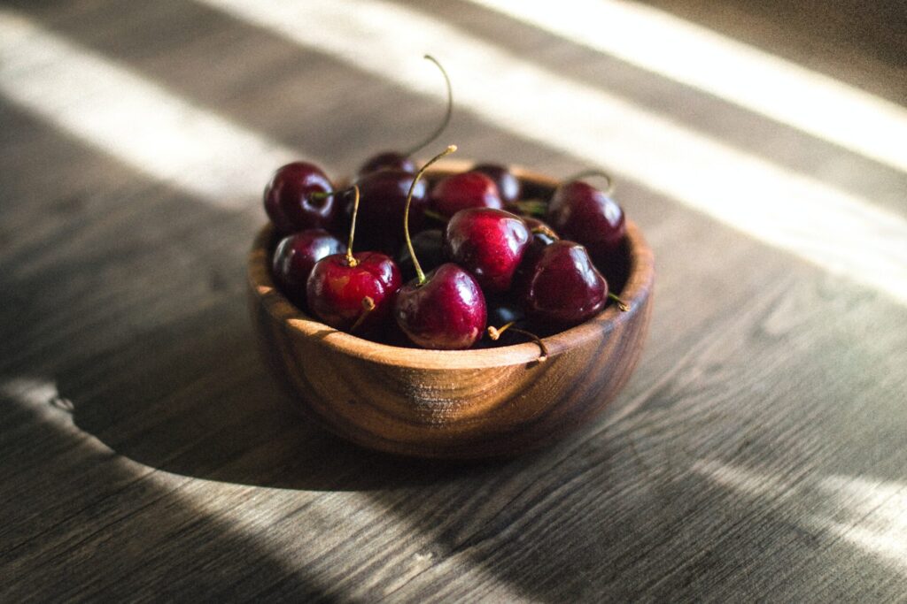 cherries in a wooden bowl atop a wooden table. 
