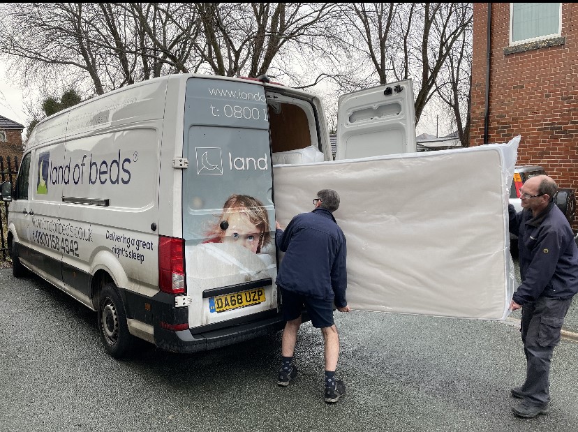 Land of Beds van with two staff lifting a mattress out the back. 